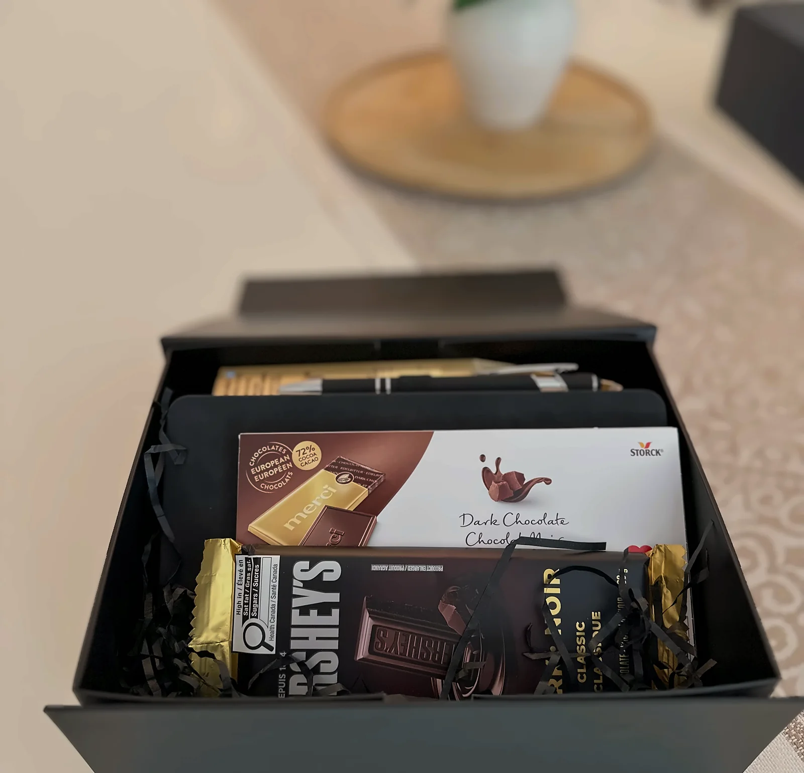A black employee gift box open on a table, set in black paper shred