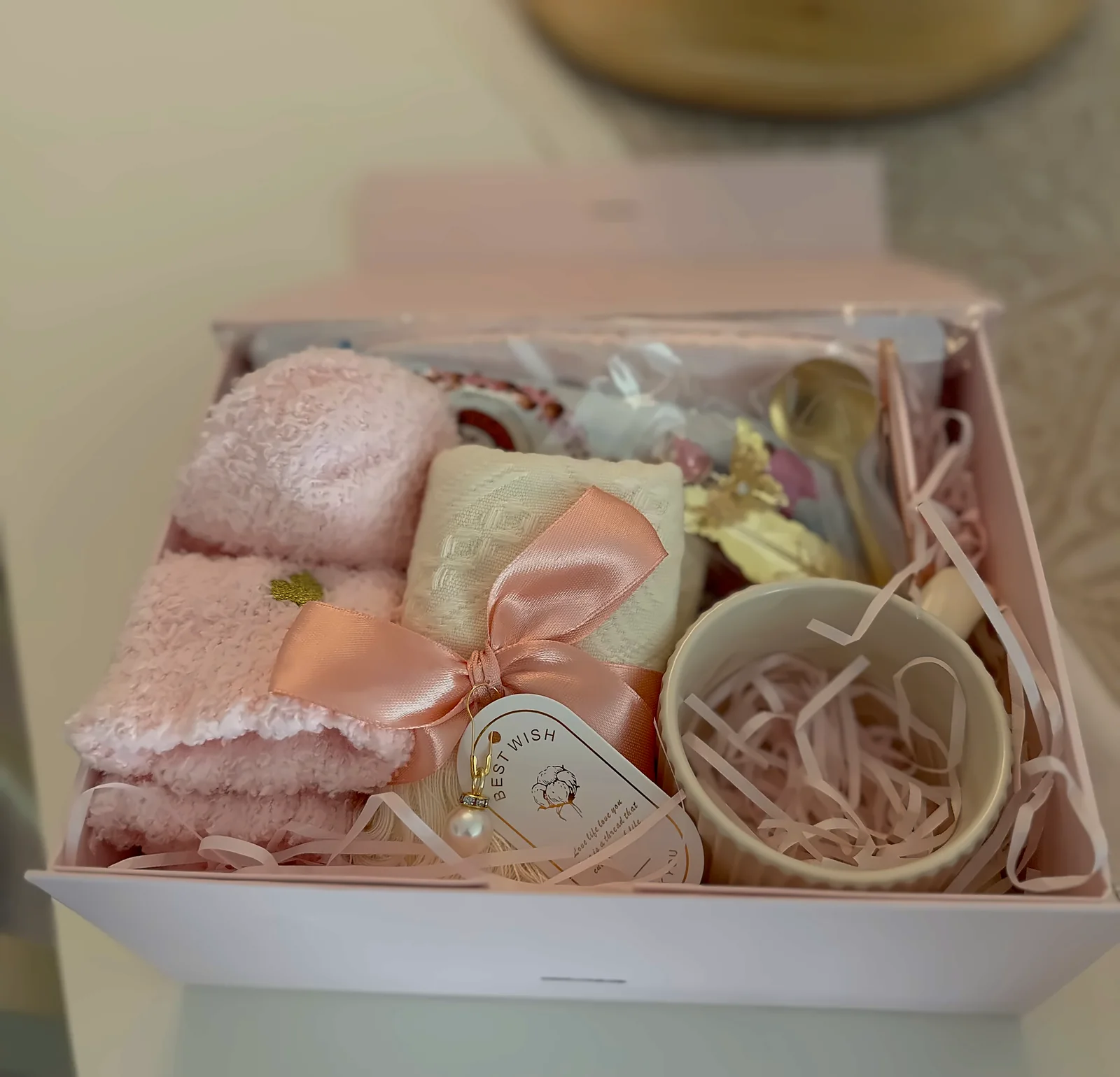 A pink employee gift box open on a table, set in rose paper shred