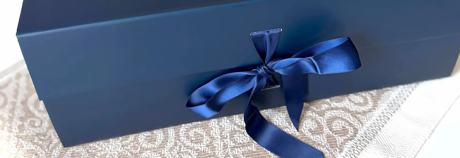 The navy box closed, a navy satin ribbon tied in a bow across the lid