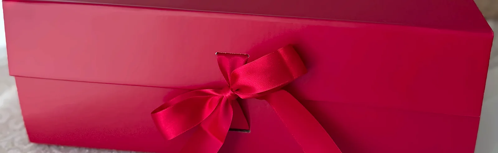 The red box closed, the red satin ribbon tied in a bow across the lid seam